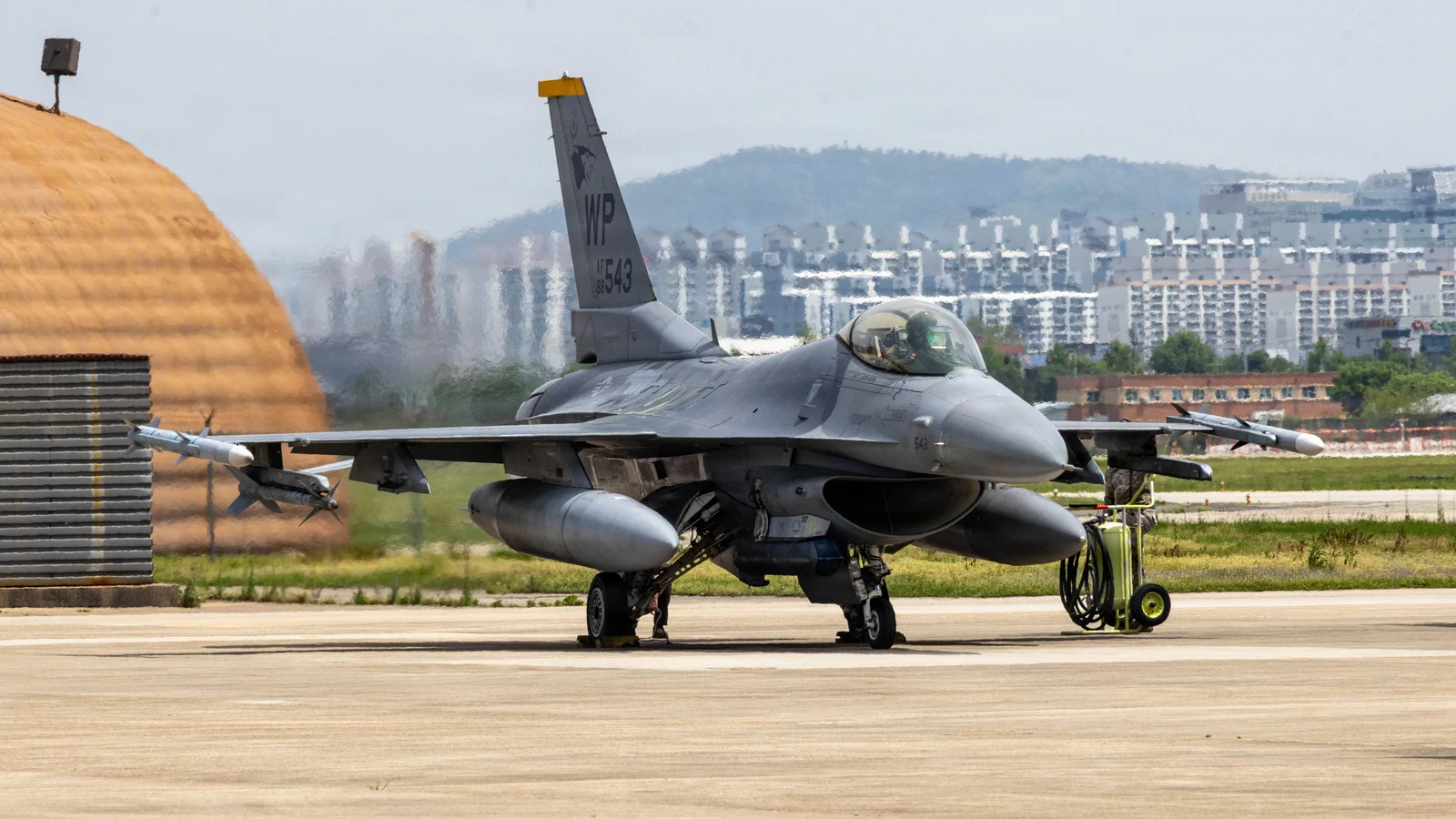 A fighter jet on the flight line at Gwangju Air Base, with apartment buildings in Gwangju behind it