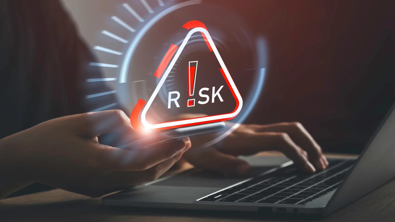 A red warning triangle reading RISK glows over a person using a laptop, illustrating AI risk.
